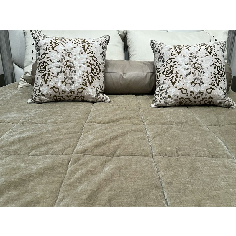 Beige quilted comforter and patterned pillows on a bed